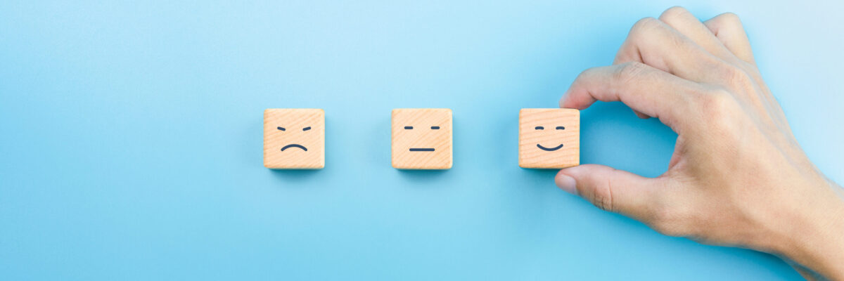 Customer service evaluation and satisfaction survey concepts. The client's hand picked the happy face smile face icon on wooden cubes on blue background